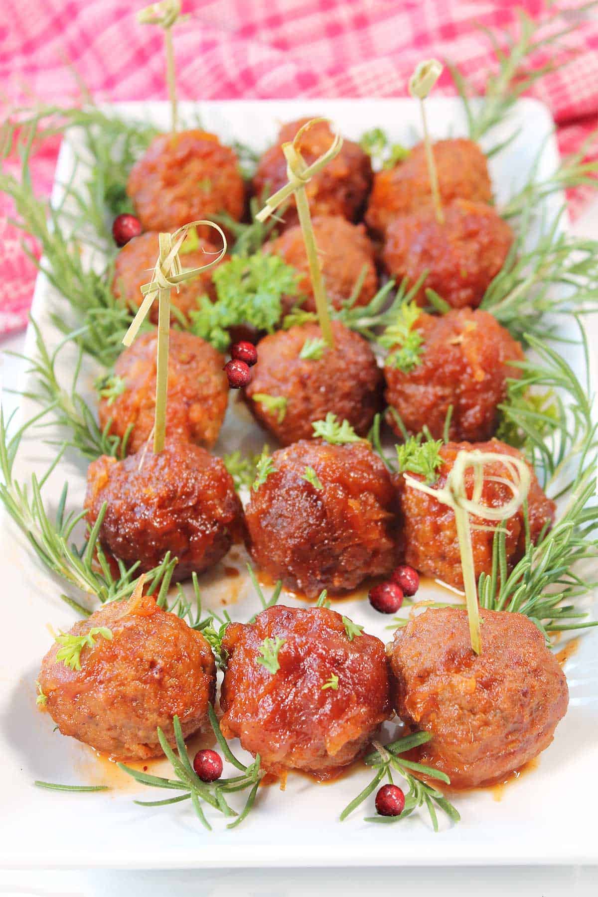 Cranberry meatballs with chili sauce on plate garnished with rosemary and cranberries.
