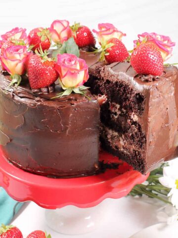 Lifting slice of chocolate cake with strawberries out of full cake.