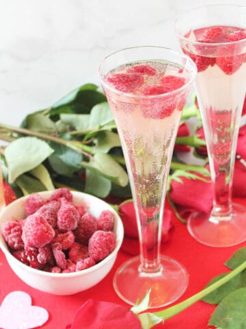 Two glasses of spritzer on red Valentine heart with rose and raspberries.
