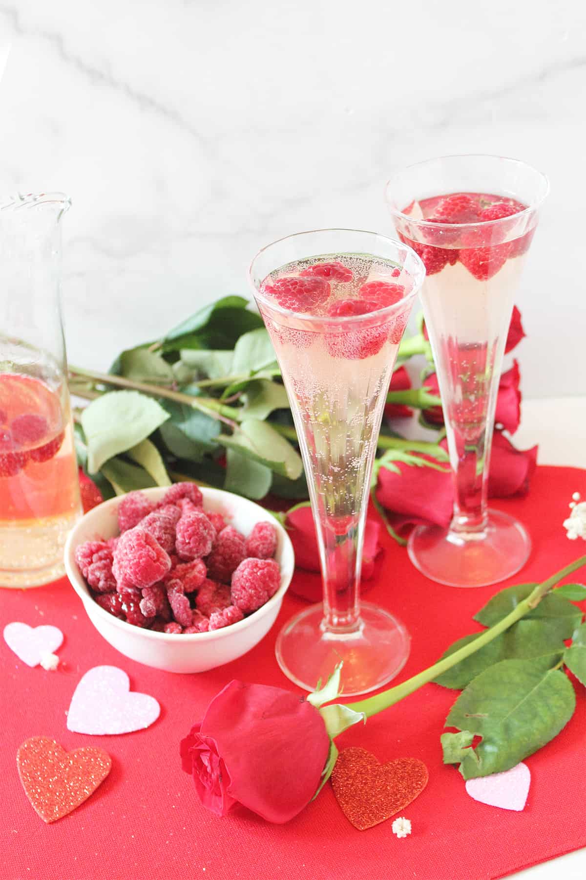 Two glasses of Valentine's Day white wine spritzer ocktail on red heart with raspberries and roses.