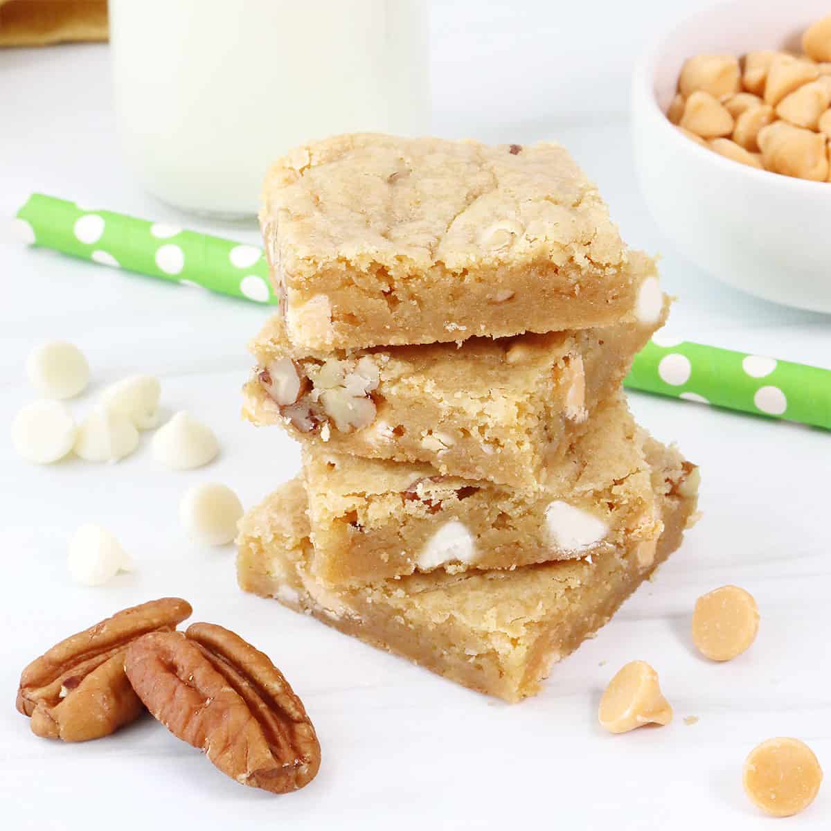 Stacked butterscotch blondies with white chocolate chips and nuts around.