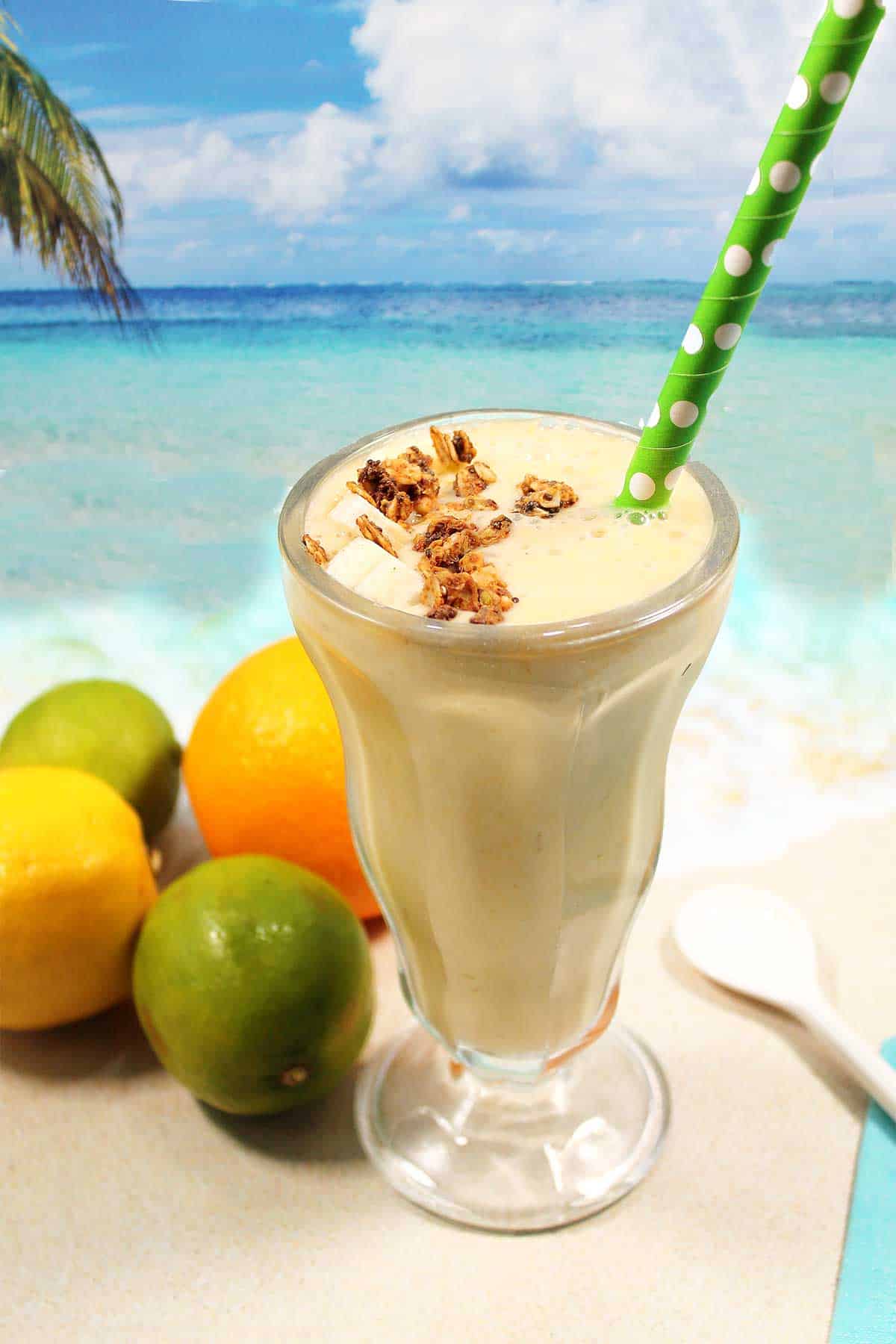 Citrus Smoothie in a glass with granola and a straw.