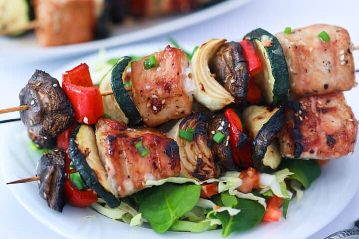 Closeup of 2 grilled pork kabobs on top of salad.