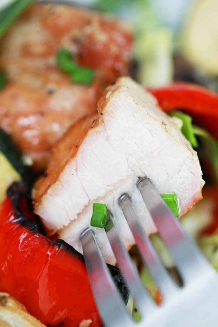 Closeup of bite of pork on fork over kabobs.