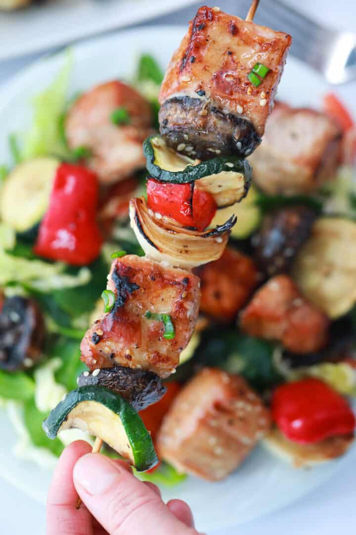 Holding grilled pork kabob over salad.