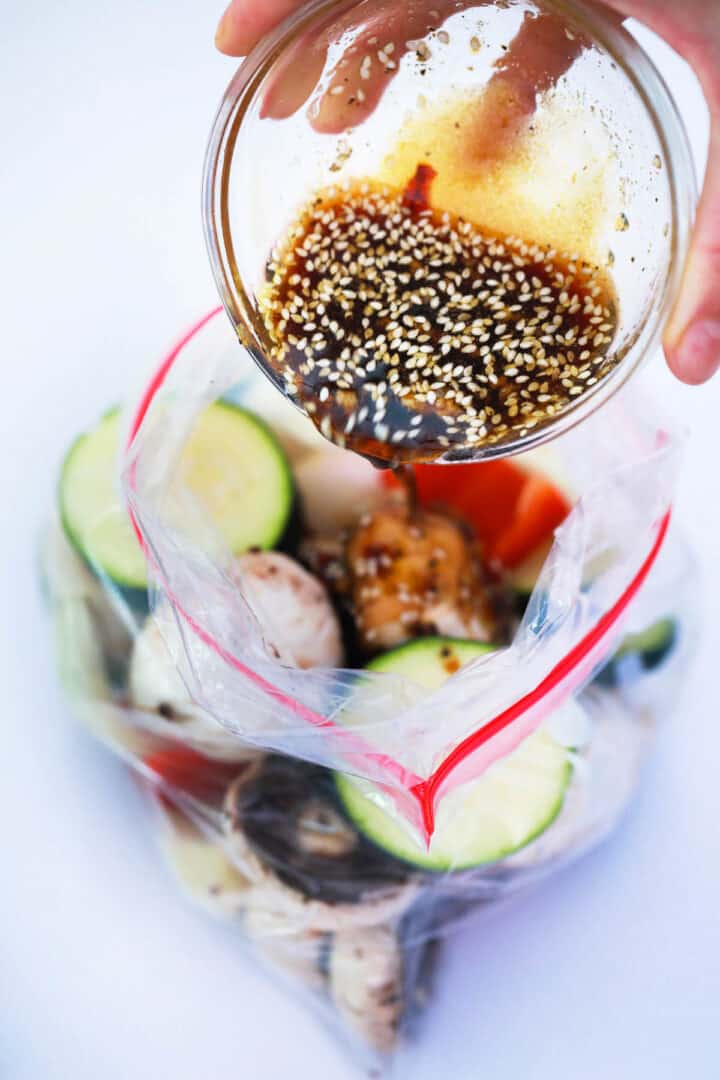 Pouring marinade over vegetables in plastic bag.