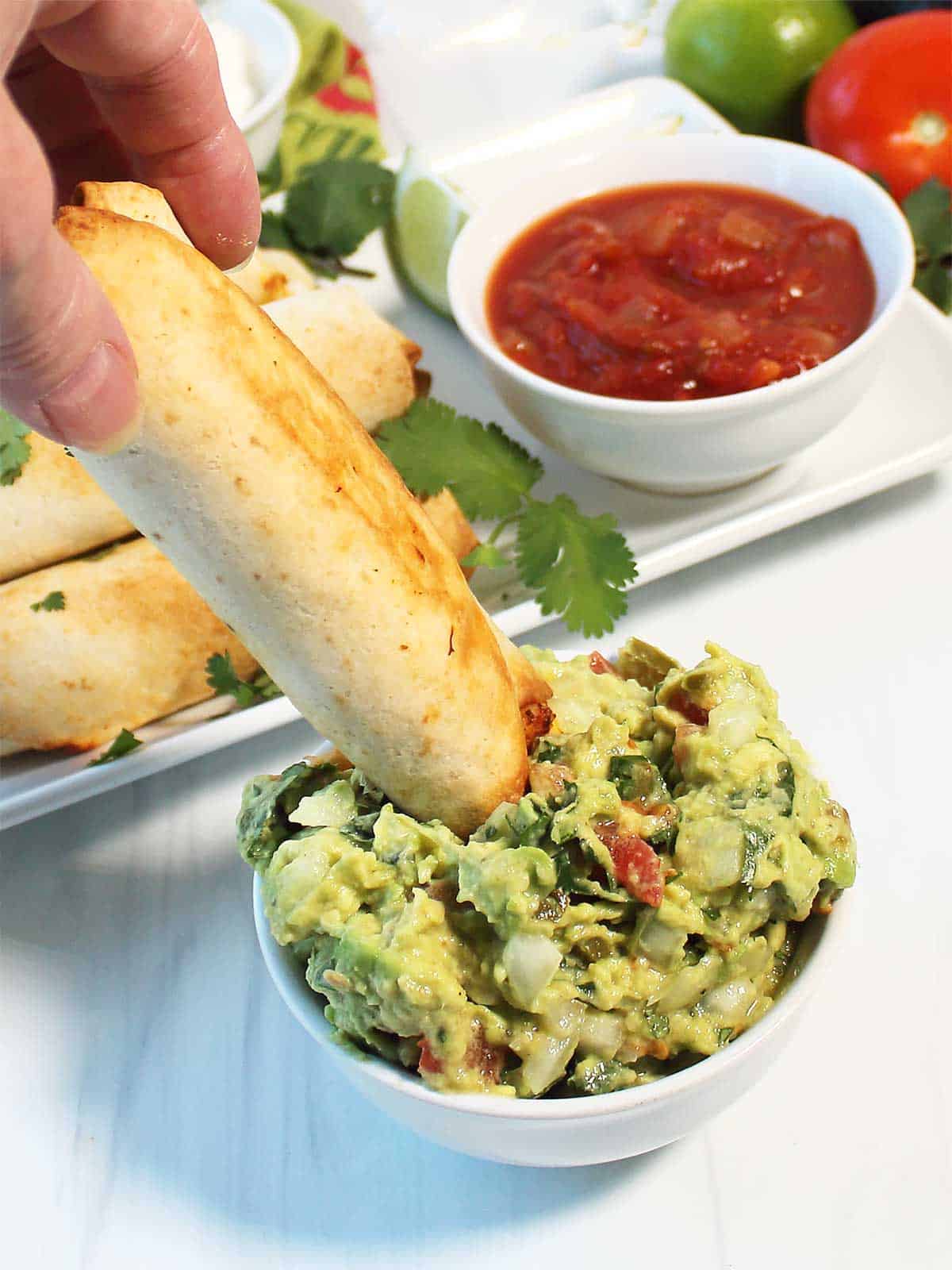 Dipping air fried taquitos into guacamole.