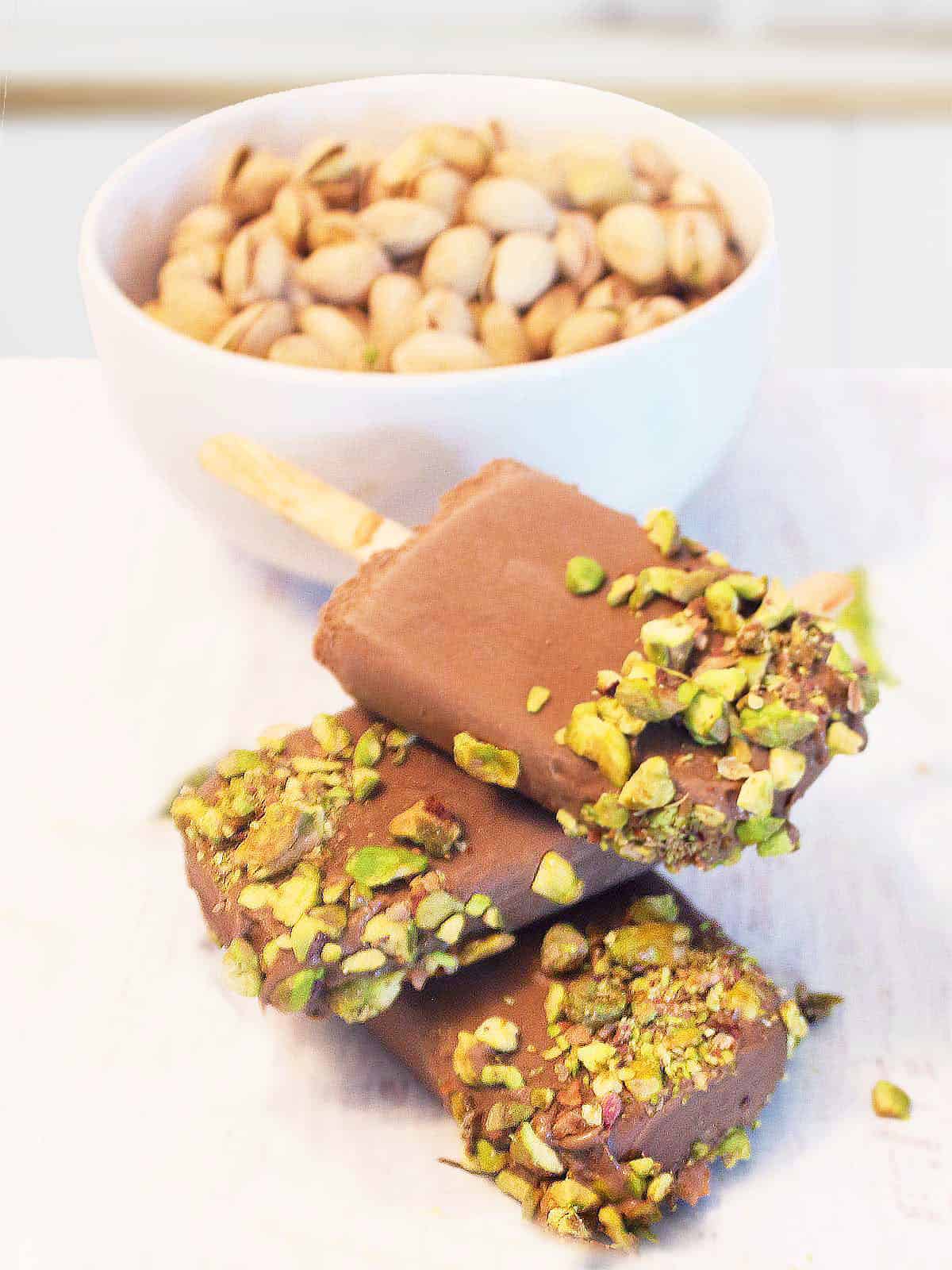 Stack of chocolate pistachio popsicles with bowl of pistachios.