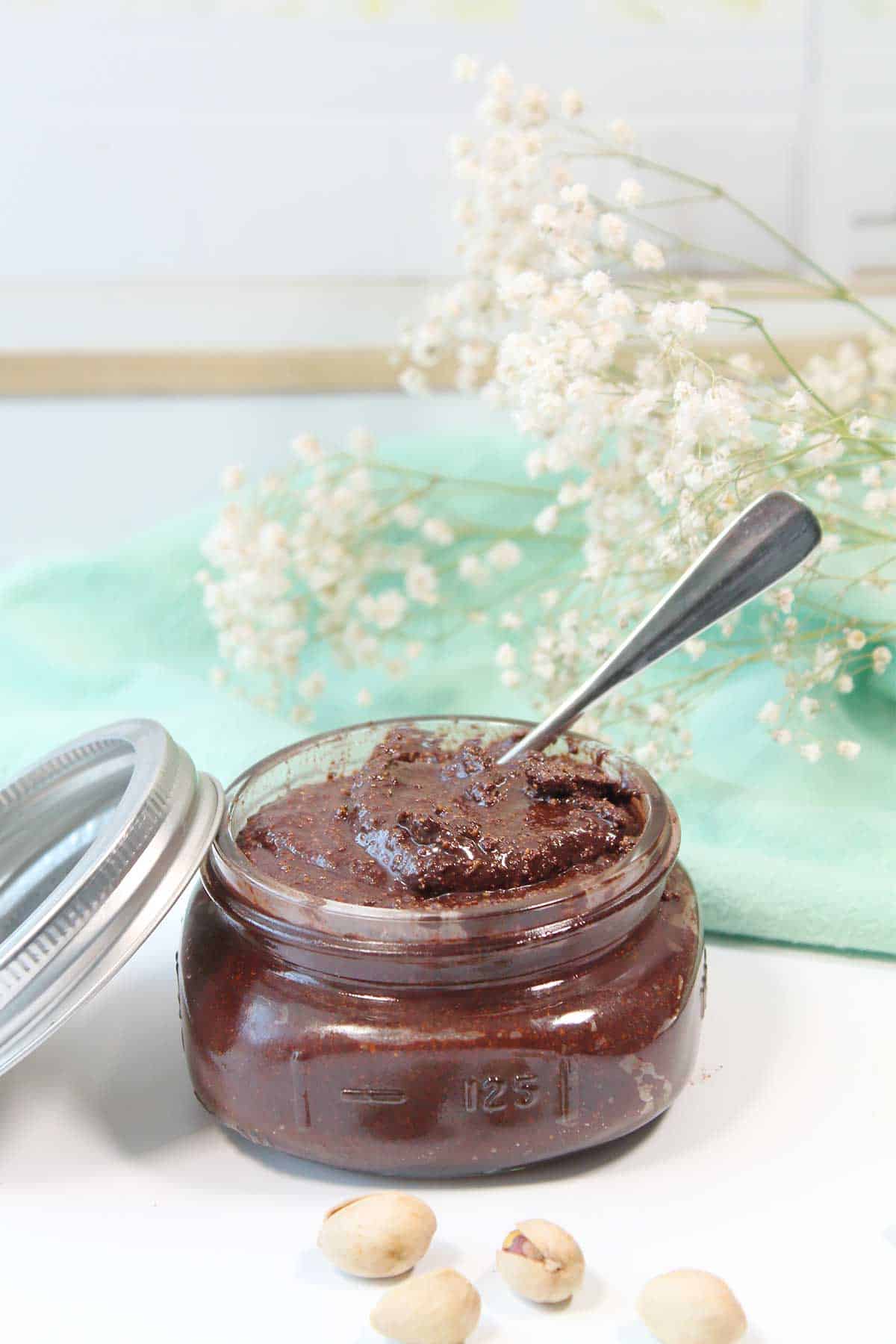 Jar of chocolate pistachio spread with spoon in it.