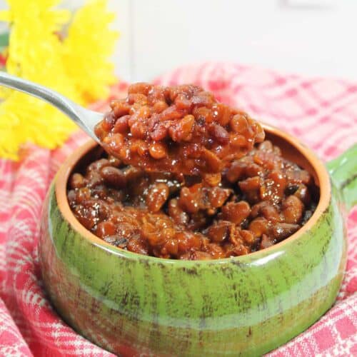 Spoonful of crockpot bourbon baked beans over bowl.