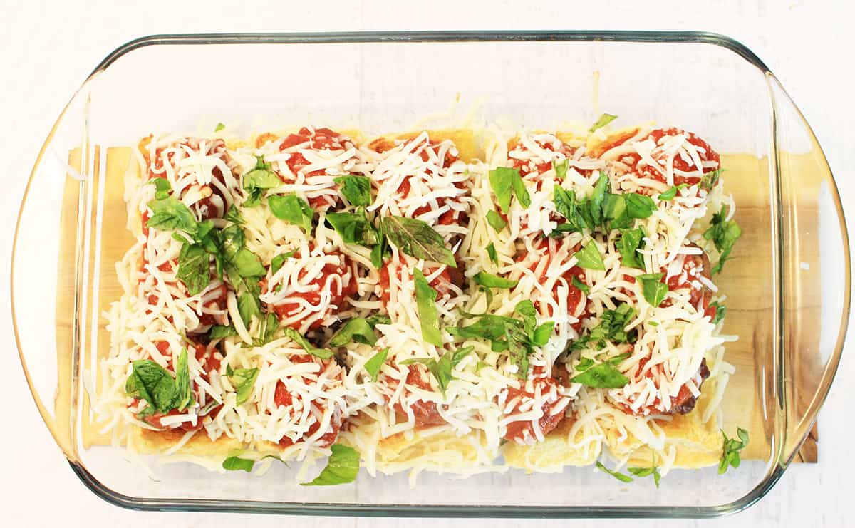 Meatballs in baking dish sprinkled with cheese and basil.