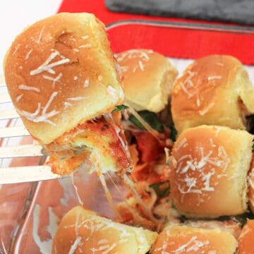 Lifting meatball slider on Hawaiian roll out of baking dish.