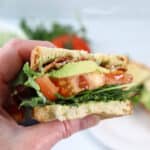 Holding halved spicy BLT sandwich.