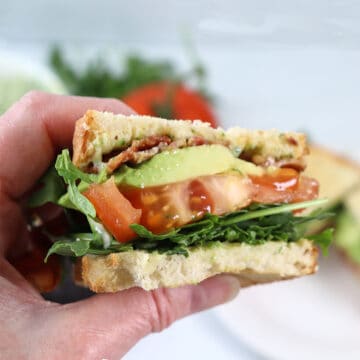 Holding halved spicy BLT sandwich.