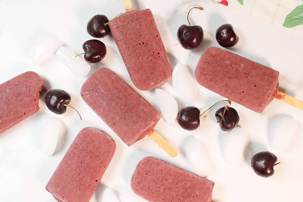 Yogurt popiscles scattered on white table with ice cubes and cherries.