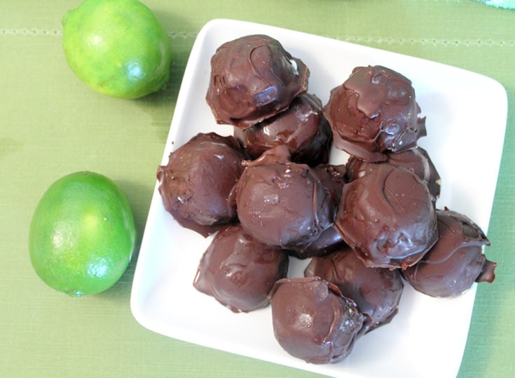 Overhead of frozen chocolate covered key lime bites on white plate with limes.