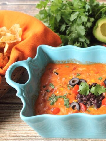 Spicy cheese dip in casserole dish garnished with olives and cilantro.