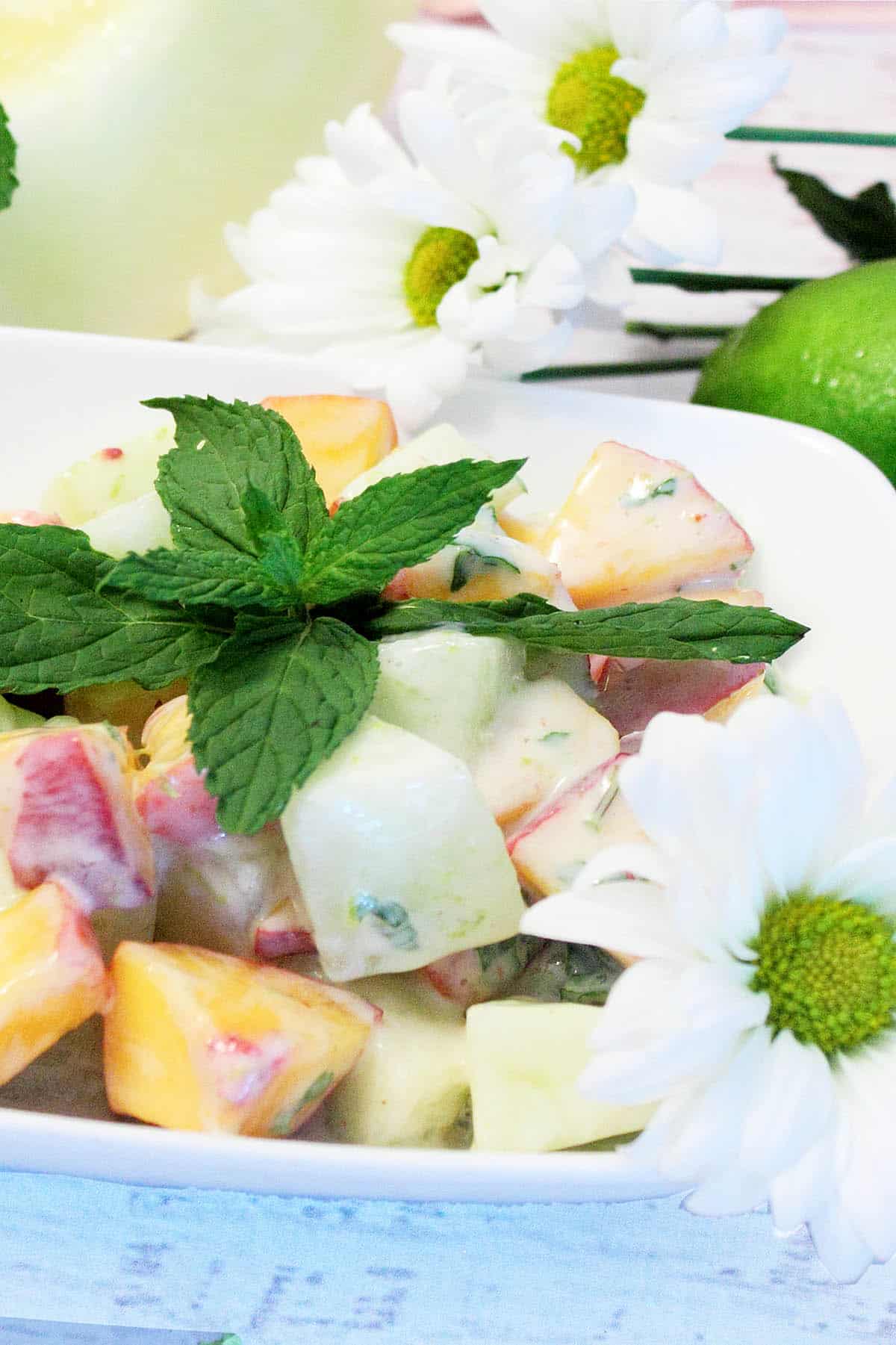 closeup of salad in white bowl with daisies behind it.