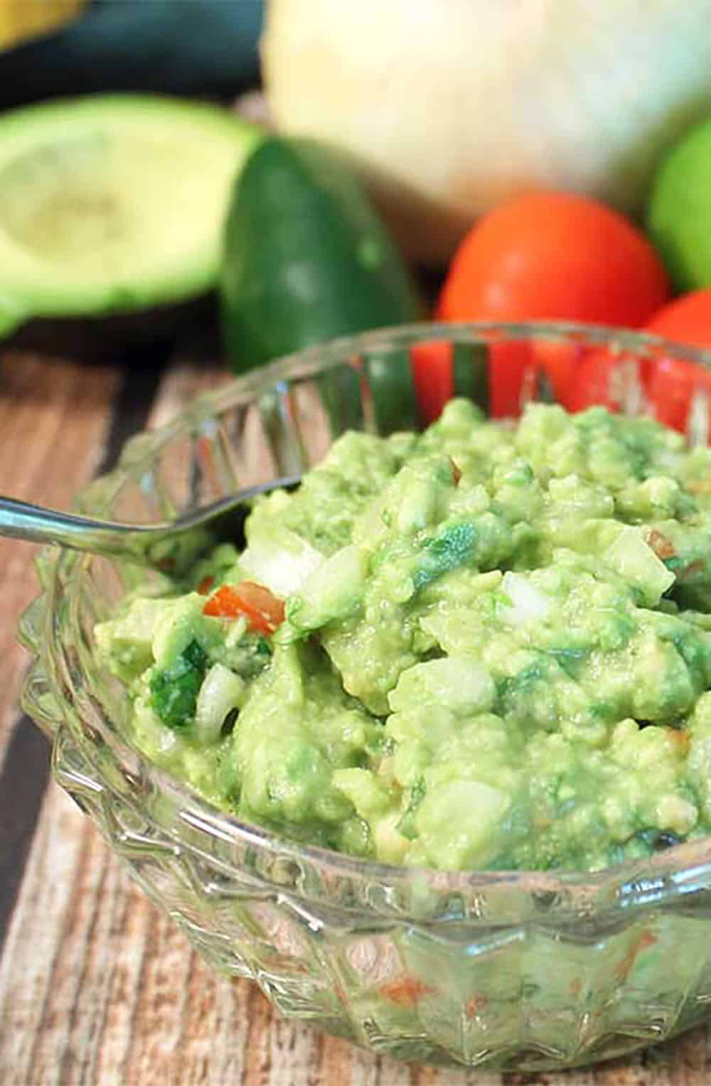 Bowl of guacamole closeup with ingredients in background.