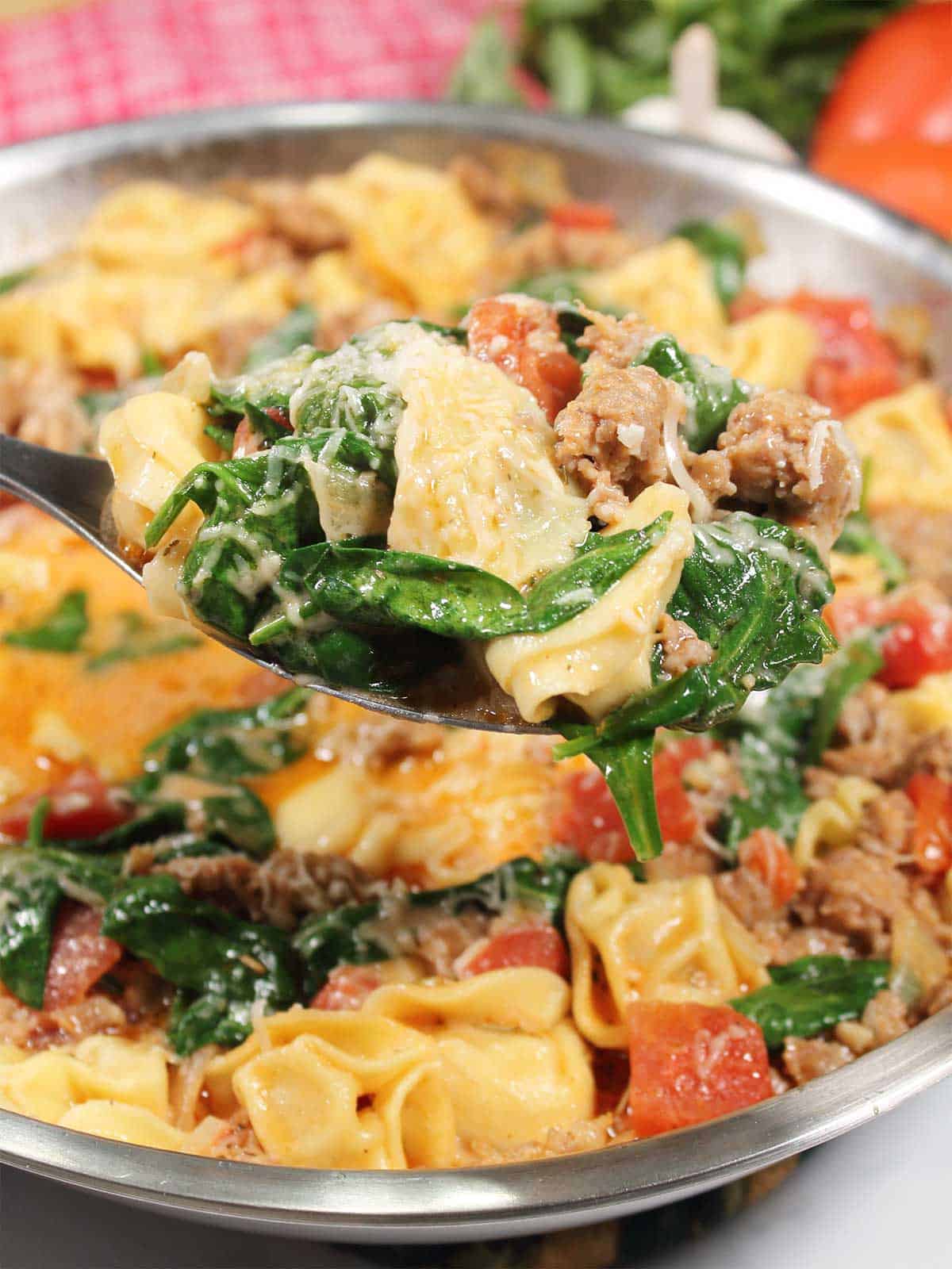 Spoonful of tortellini showing sausage and spinach.