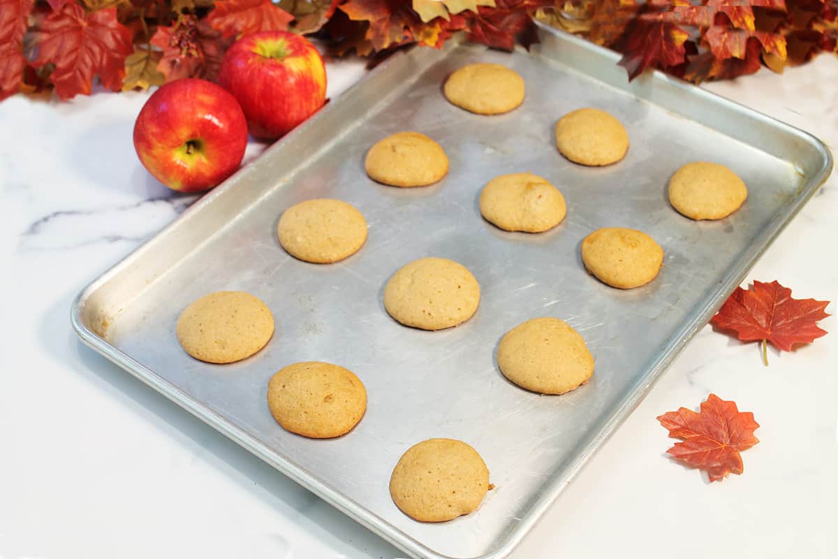 Tray of baked apple cider cookies on white table with apples.