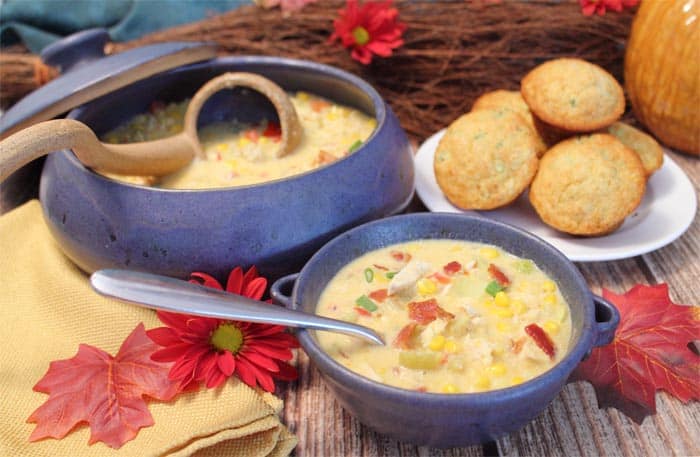 Corn chowder in blue bowl with corn muffins and larger bowl with ladle.