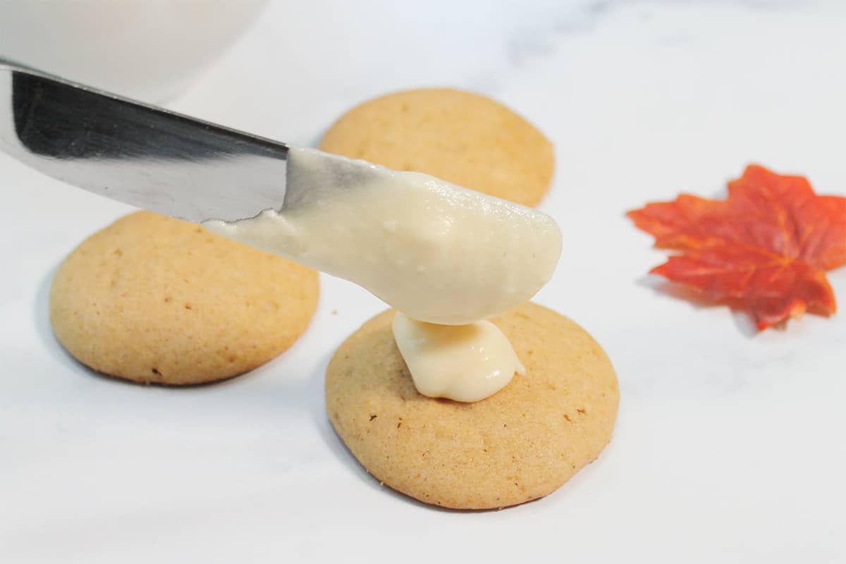 Frosting cookies and spreading with a knife on white table.