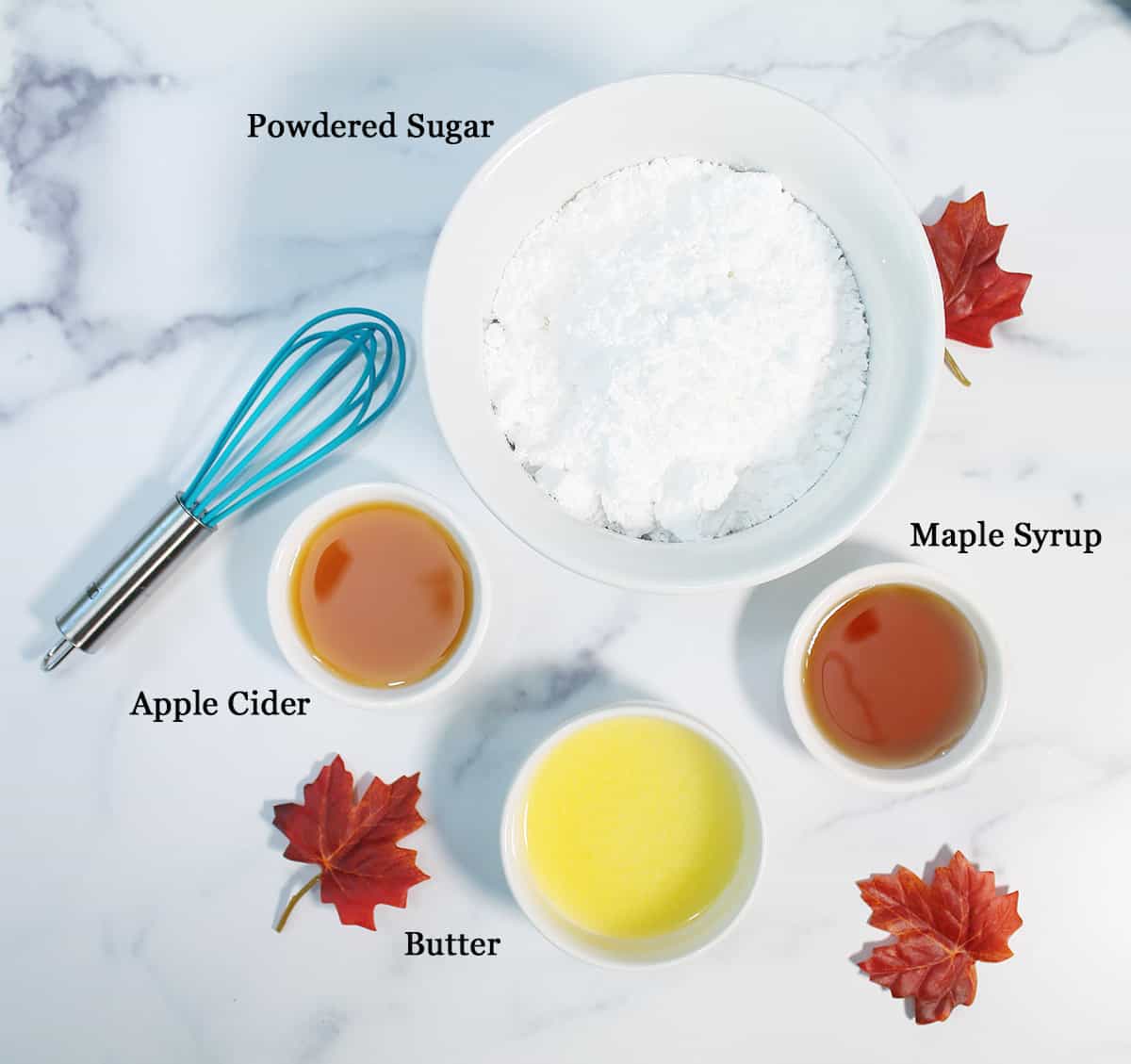 Ingredients for maple frosting on white table with whisk.