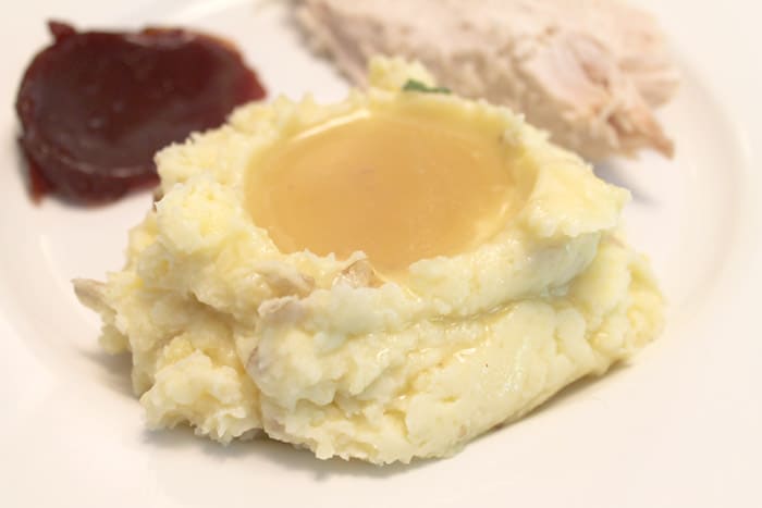 Mashed Potatoes with gravy on top on full Thanksgiving dinner plate.