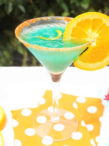 Single curacao cocktail on orange polka dotted napkins.