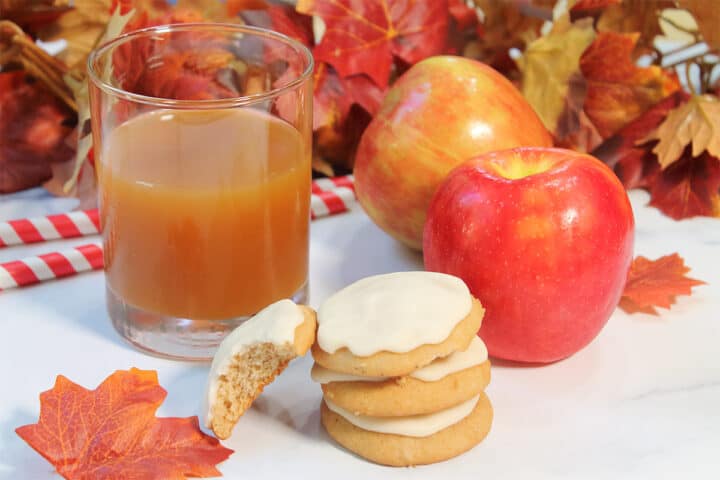 Stack of cookies by cider, apples and fall leaves.