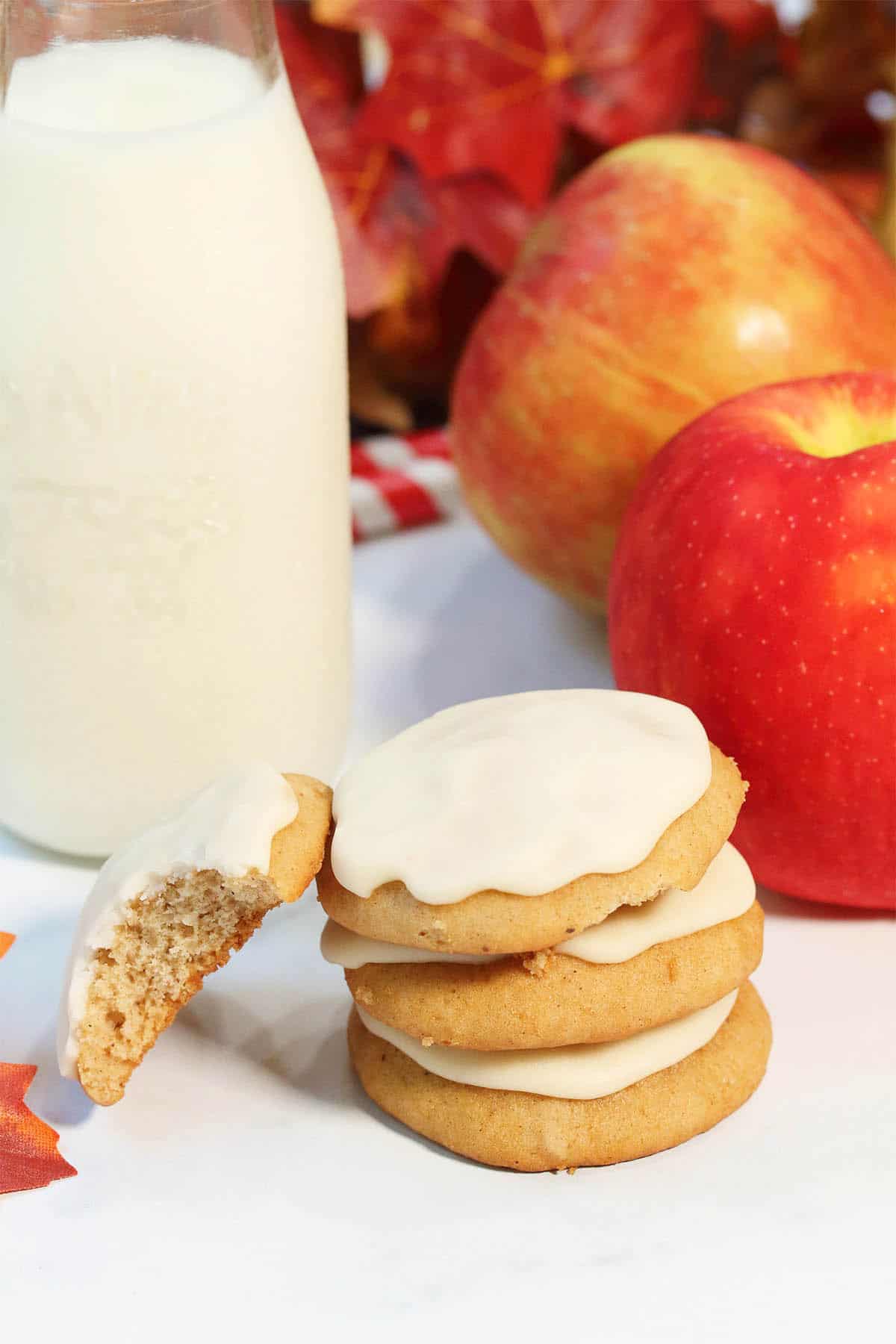 Stack of cookies with milk bottle and apples on white table.