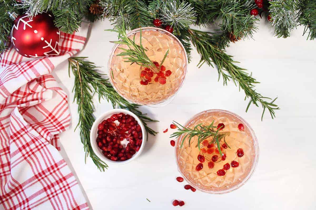 Two cocktails with pomegranate arils and rosemary sprigs.
