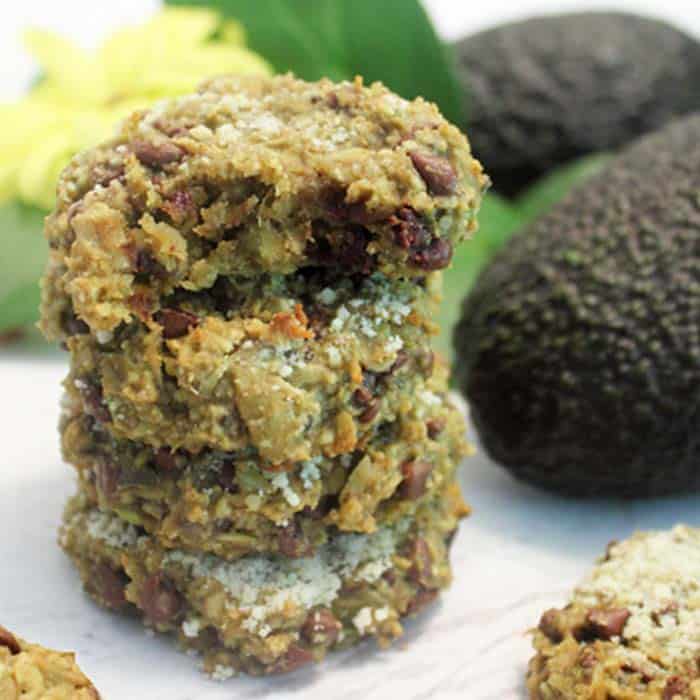 Stacked oatmeal cookies on white table with avocado next to them.