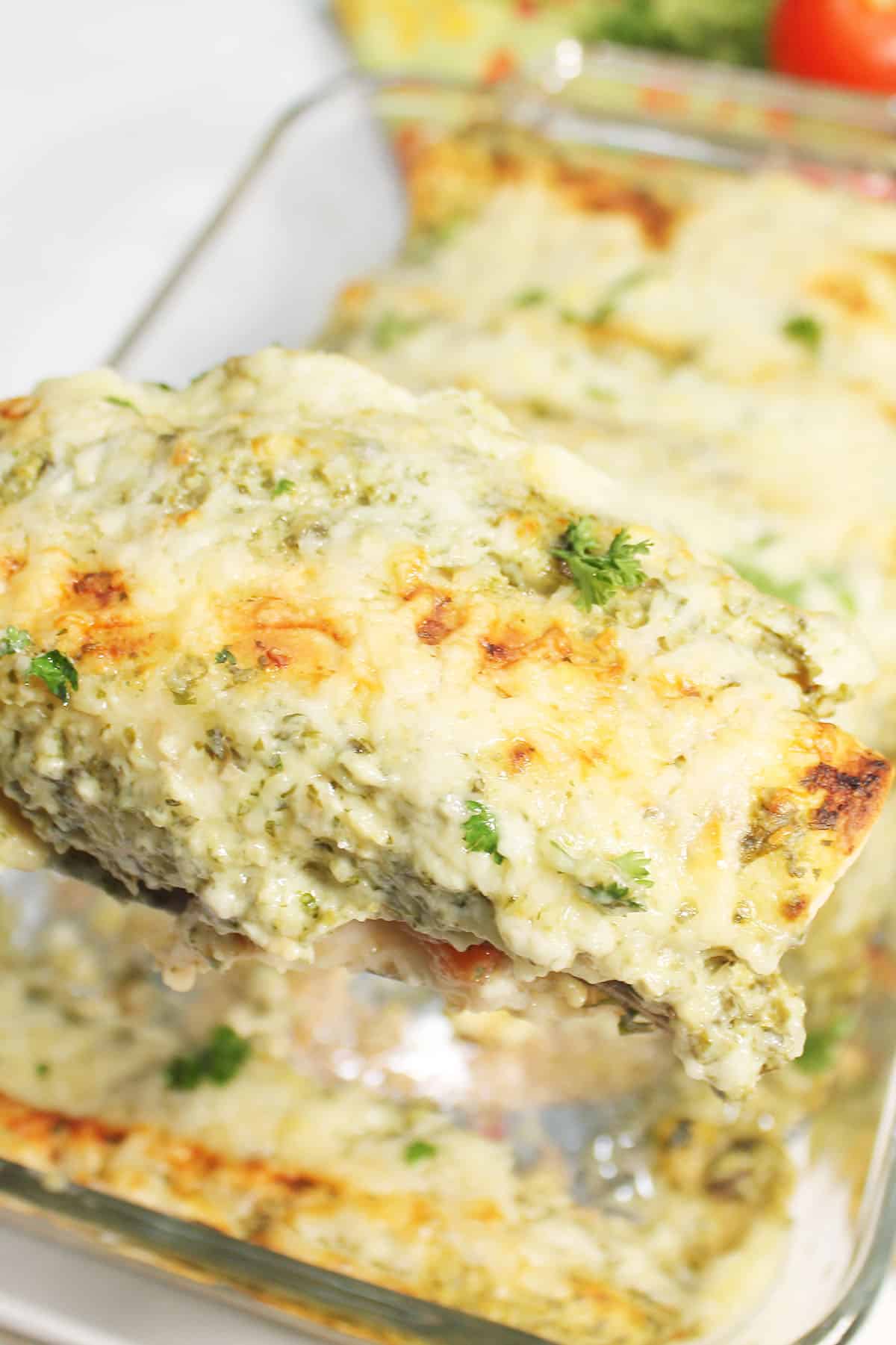 Lifting a serving of enchiladas with green sauce out of the baking dish.