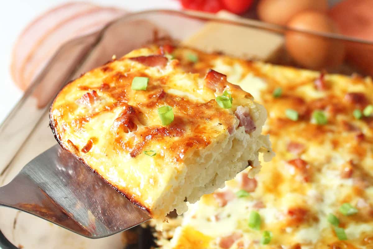 Lifting serving of breakfast casserole with ham out of baking dish.