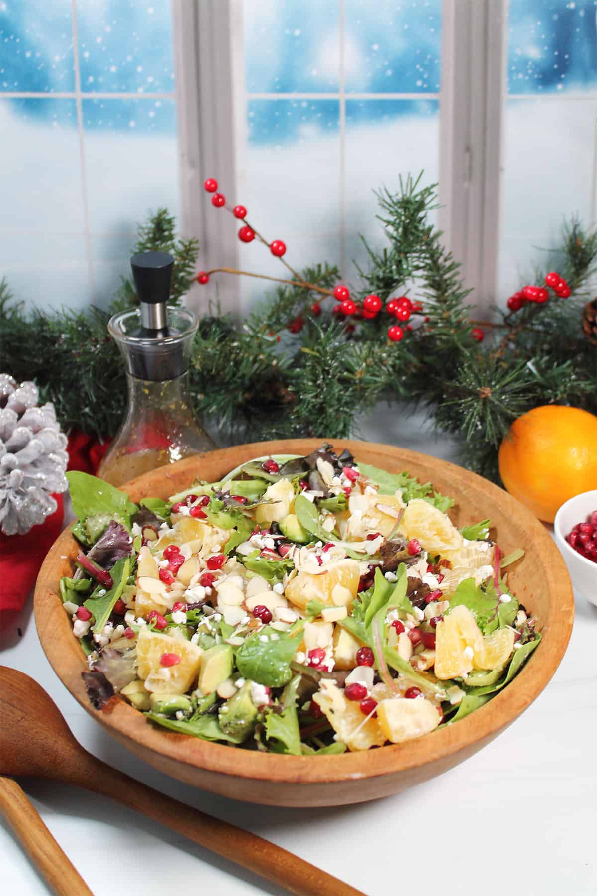 Tossed Orange Pomegranate Salad in a bowl with greenery in back.