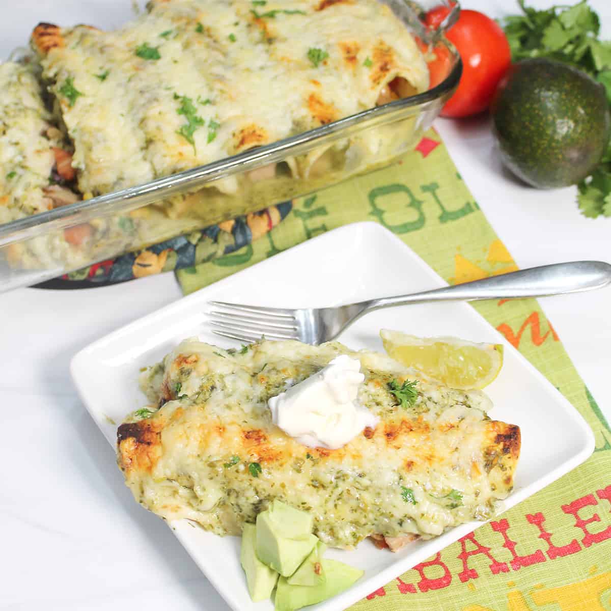Plated pork enchiladas with bite on fork and casserole in back.