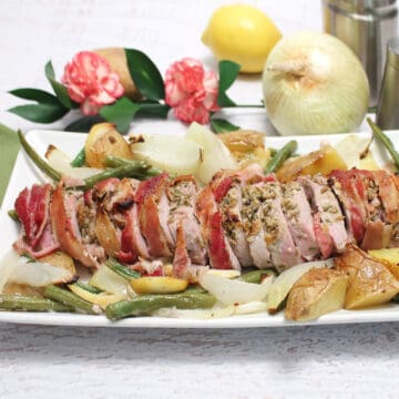 Sliced pork on white platter with vegetables.