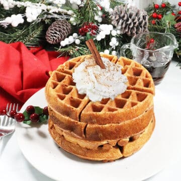 Eggnog Waffles stacked on a plate with whipped cream.