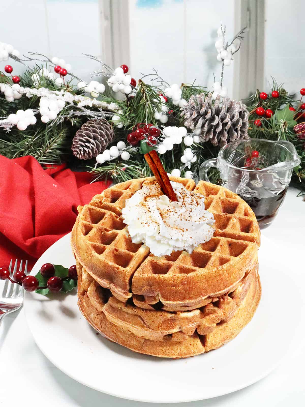 Stacked eggnog waffles with whipped cream and a cinnamon stick.