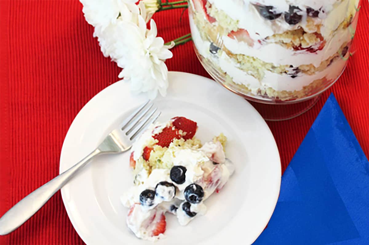 Mixed Berry Trifle serving on white plate with whole trifle in background.
