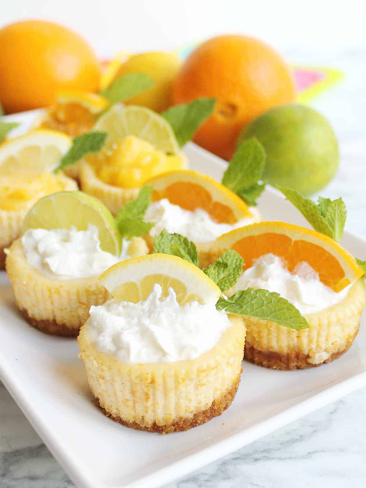 Mini Citrus Honey Cheesecakes with whipped cream and fruit garnish on platter.