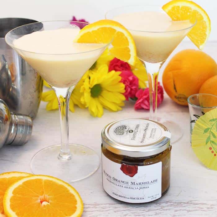 whipped martini with a garnish of orange slice, a cocktail shaker in back and orange marmalade in front