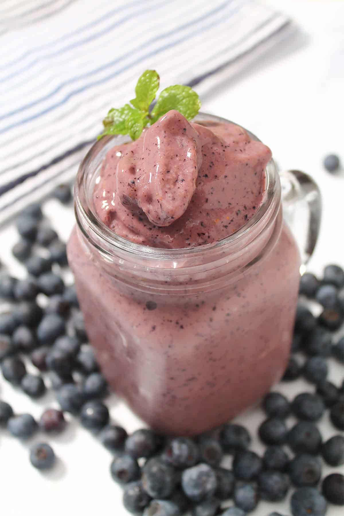 Smoothie in mason jar with mint sprig and blueberries on table.