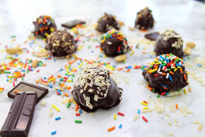 Ice Cream Truffles on white table showing sprinkled with nuts, coconut and sprinkles.