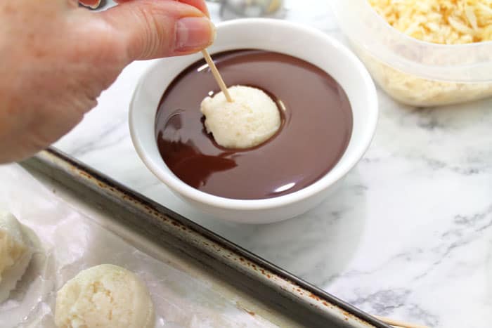 Dipping frozen ice cream ball on a toothpick into warm melted chocolate.