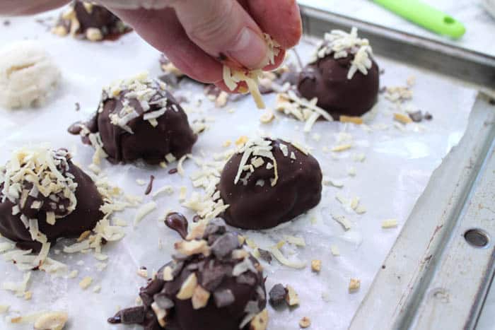 Sprinkling warm chocolate covered bites with toasted coconut.