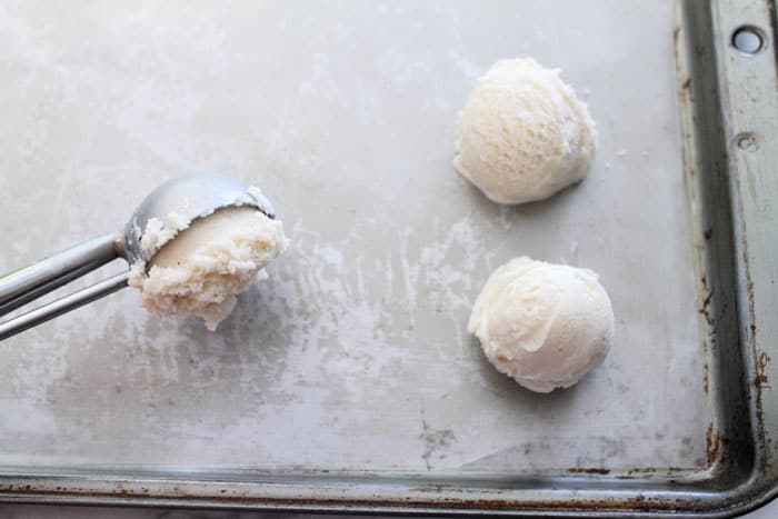 Scooping frozen ice cream into balls and placing on wax paper-lined cookie sheet.