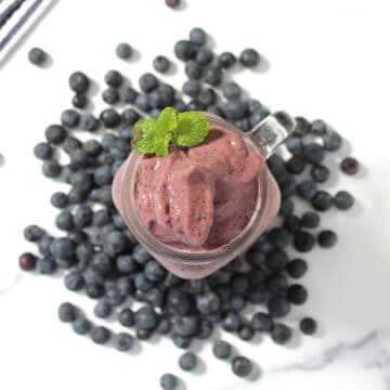 Overhead of blueberry coffee protein smoothie amid blueberries on white table.